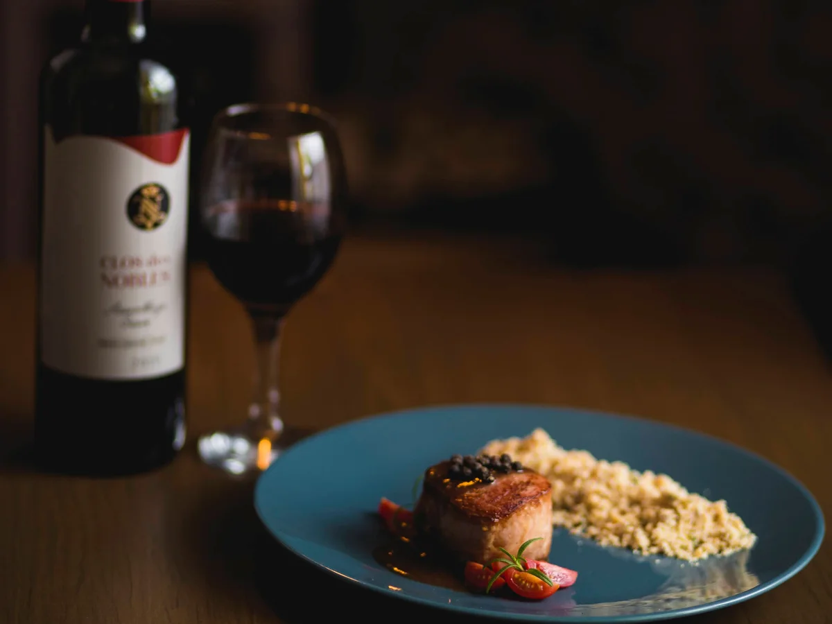 Prato servido ao lado de uma garrafa e uma taça de vinho tinto