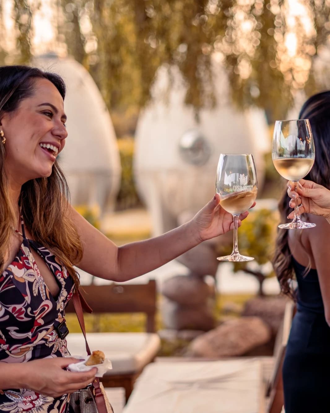 Mulher sorrindo brindando com uma taça de vinho branco ao ar livre